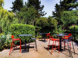 a group of tables and red chairs in a garden at ibis Metz Nord in Woippy