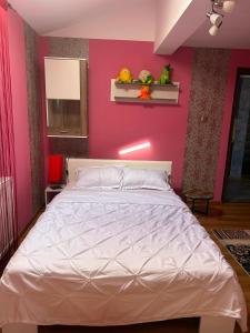 a bedroom with a white bed with a pink wall at Colț de rai - camera de inchiriat in Reşiţa