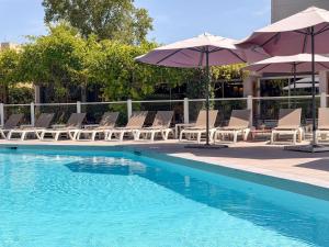 a swimming pool with lounge chairs and umbrellas at ibis Nîmes Ouest - A9 in Nîmes