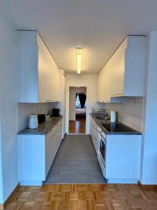 a white kitchen with white cabinets and a wooden floor at Basic Apartment in Witikon district in Zurich +16 photos