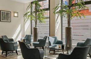 a waiting room with chairs and tables and trees at Leonardo Hotel München City Center in Munich