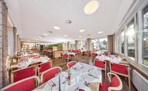 a restaurant with white tables and red chairs at Kneippkurhaus St Josef in Bad Wörishofen