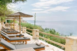 Eine Reihe Liegestühle, ein Sonnenschirm und das Meer in der Unterkunft Hotel Cokkinis in Megara
