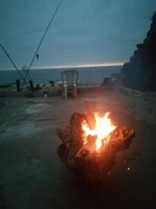 a campfire on a beach with a chair and the ocean at Grotte de pêcheurs Tigri in Aglou +5 photos