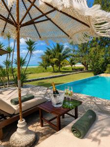 a table with wine glasses and an umbrella next to a pool at Villa Cote Sud Pousada De Charme - Pé na Areia in São Miguel dos Milagres