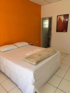 a large white bed in a room with an orange wall at Golden Stay Suites in Jacareí