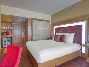 a bedroom with a large bed and a red chair at Novotel Bengaluru Outer Ring Road in Bangalore