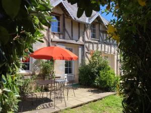 a table and chairs with an umbrella in front of a house at GITE EQUESTRE DE LA LANDE in Bréhal