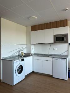 a kitchen with white cabinets and a washer and dryer at Apartamentos El Jardín de Isla Autocheck-In in Isla