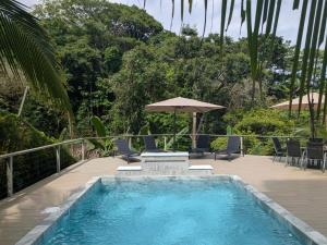 a swimming pool with chairs and an umbrella at Villa Costa Vida Tower Suites in Quepos