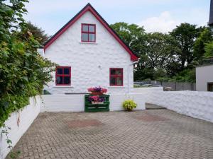 a white house with red windows and flowers in a courtyard at Central Dingle Cottage in Dingle