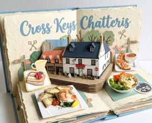 a book with a model of a house and food at Cross Keys Hotel Chatteris in Chatteris