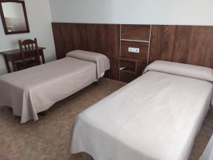 two beds in a room with a desk and a chair at Hostal El Polígono in Lucena