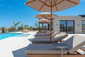 a row of chairs with umbrellas next to a swimming pool at Nysa Luxury villas 3-4-5-6 in Heraklion