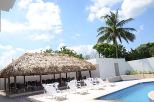 a group of chairs and a swimming pool with a straw umbrella at San Jeronimo Hotel in Dibulla