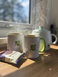 two coffee mugs sitting on a table next to a window at Blackthorn and Rose Shepherds Huts in Scribbagh