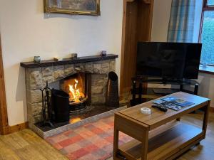 a living room with a fireplace with a television and a table at Burnside Holiday Cottage 2 in Fochabers