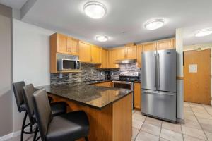 a kitchen with wooden cabinets and a stainless steel refrigerator at Woodrun Lodge 514 | Ski-In Ski-Out Condo w/ Pool, Hot Tub, Free Parking, Wifi & Laundry in Whistler
