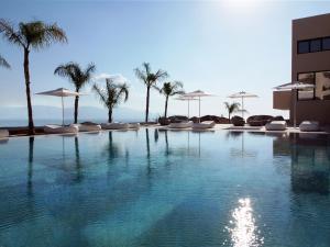 a swimming pool with chairs and palm trees and a building at Althea Resort in Áno Loutrón