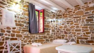 a stone walled room with two beds and a window at Rodakas Rooms-Glikeria in LivadhokhÃ³rion