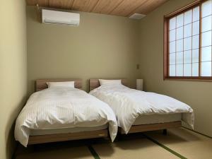 a bedroom with two beds with white sheets and a window at あわら湯のまち駅から徒歩3分の湯の花ハウス in Awara