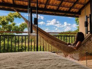 a woman sitting in a hammock on a porch at Claruá Chalés- Loft Caju- Pé direito duplo, 3min de carro do Rio- Conforto e Natureza dentro da cidade in Cavalcante