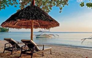 two chairs and an umbrella on a beach with a boat at easy diving and beach resort in Manlocahoc