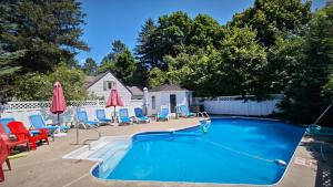 a swimming pool with chairs and umbrellas in a yard at Motel des Pentes et Suites in Saint-Sauveur-des-Monts