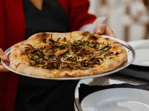 a person holding a pizza on a plate at &Tales Hotel - Óbidos in Óbidos