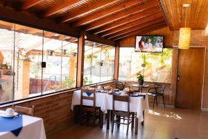 a restaurant with white tables and chairs and windows at Pousada Palma Chalés in Monte Verde