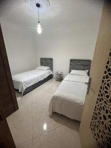 two beds in a room with white walls at Atouli Suites in Nador