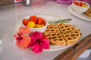 a plate with waffles and a bowl of fruit and flowers at Kalunay Hostel - Breakfast included in Puerto Viejo