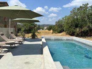 a swimming pool with an umbrella and chairs and a table at Maison éla in Bessas