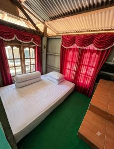 a bedroom with a bed with red curtains and a table at Sunrise Komodo Homestay in Komodo