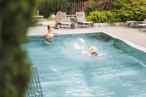 two people are swimming in a swimming pool at Sporthotel Zoll in Vipiteno