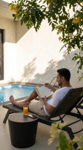a man sitting in a chair reading a book next to a pool at Hafawah Resort in Medina