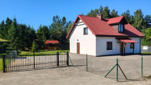 a white house with a red roof behind a fence at Biały Domek Nielbark - Agroturystyka in Nielbark