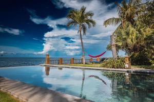 a swimming pool next to the ocean with palm trees and a hammock at Villa Seaview- tranquil 3BR, beachfront, private pool in Bukti