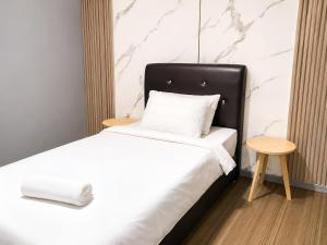 a white bed with a black headboard and a wooden stool at Neela Homestay in Labuan