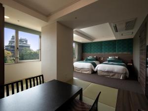 熊本市にあるKKRホテル熊本のベッド2台とダイニングテーブルが備わるホテルルームです。