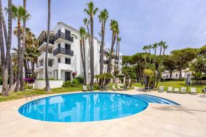a swimming pool in front of a building with palm trees at Jardines de las Golondrinas in Marbella