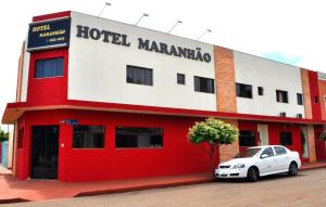 un edificio rojo y blanco con un coche blanco aparcado delante en Hotel Maranhão, en Ourinhos