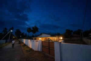 a man walking down a street next to a fence at night at Rani Alfred in Viramanikkatevanturai
