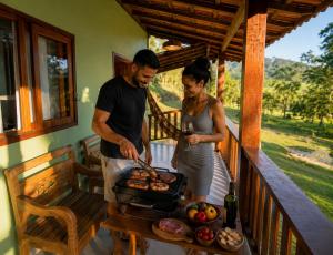 a man and woman cooking on a grill on a porch at Chalé Céu de Minas in Visconde De Maua +38 photos