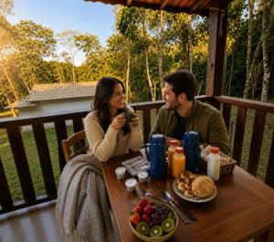 a man and woman sitting at a table with food at Chalé Céu de Minas in Visconde De Maua