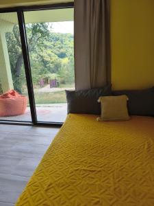 a bedroom with a yellow bed with a large window at Iza sedam gora in Rakovac