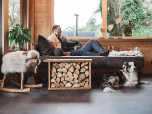 Ein Paar sitzt mit zwei Hunden auf einem Sofa. in der Unterkunft Romantikchalet Fuchsbau mit eigenen Wellnessbereich, Komfort und viel Ruhe in der Natur in Vorra
