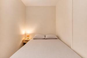 a small white bedroom with a bed and a nightstand at Charmant appartement proche Val Europe Disneyland paris in Torcy