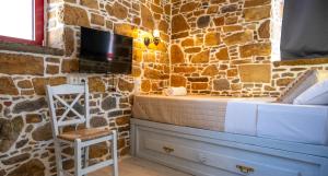 a bedroom with a stone wall with a bed and a chair at Rodakas Rooms-Danae in LivadhokhÃ³rion