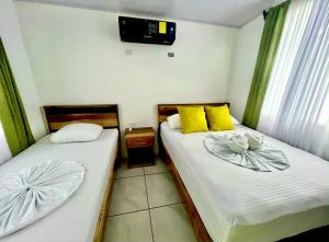 two beds in a room with a tv on the wall at Casa Caribe in Tortuguero